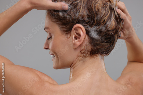 Woman washing hair on light grey background, back view