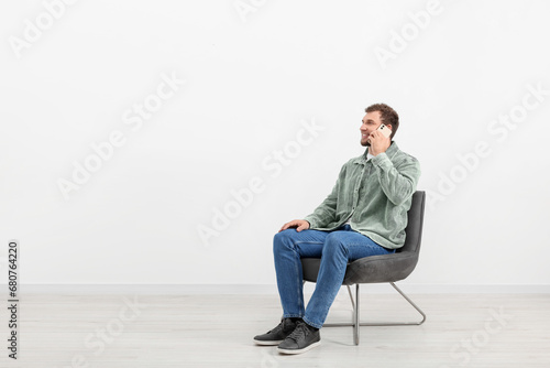 Young man talking on smartphone while sitting on chair indoors. Space for text