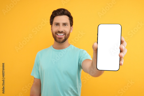 Handsome man showing smartphone in hand on yellow background, selective focus. Mockup for design photo