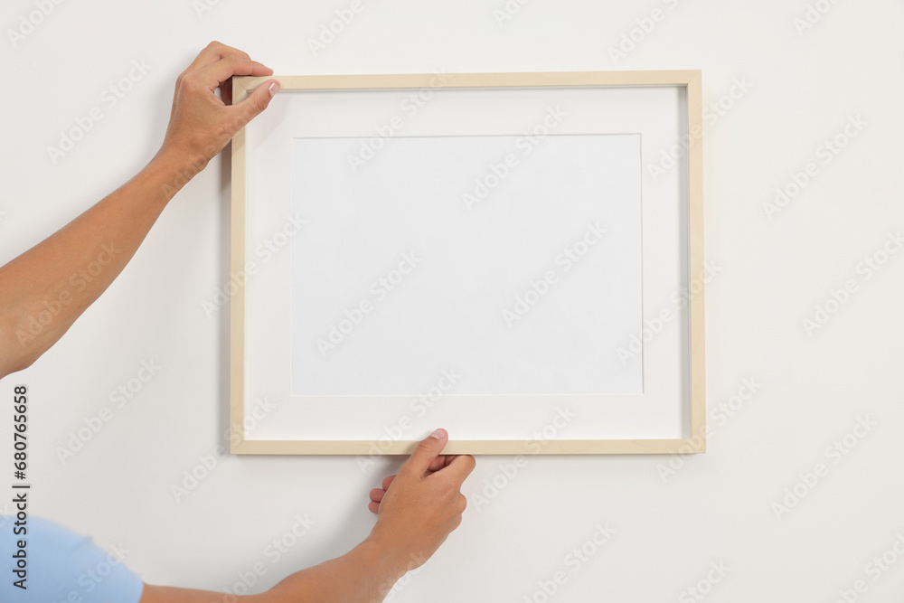 Obraz premium Young man hanging picture frame on white wall indoors, closeup