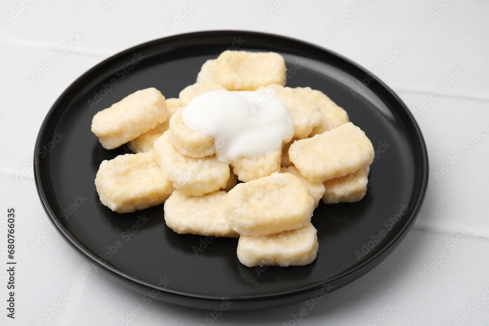Plate of tasty lazy dumplings with sour cream on white tiled table Plate of tasty lazy dumplings with sour cream on white tiled table