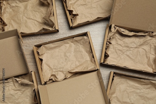 Many open cardboard boxes with crumpled paper on wooden background, flat lay