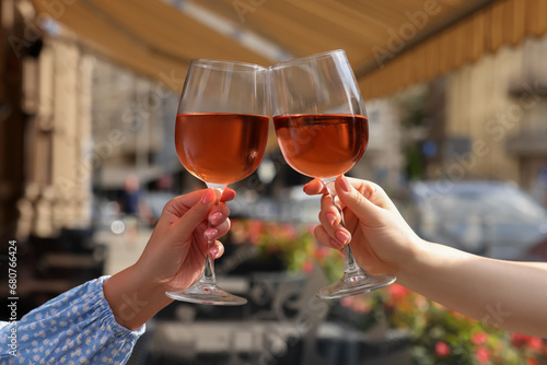 Women clinking glasses with rose wine in outdoor cafe, closeup
