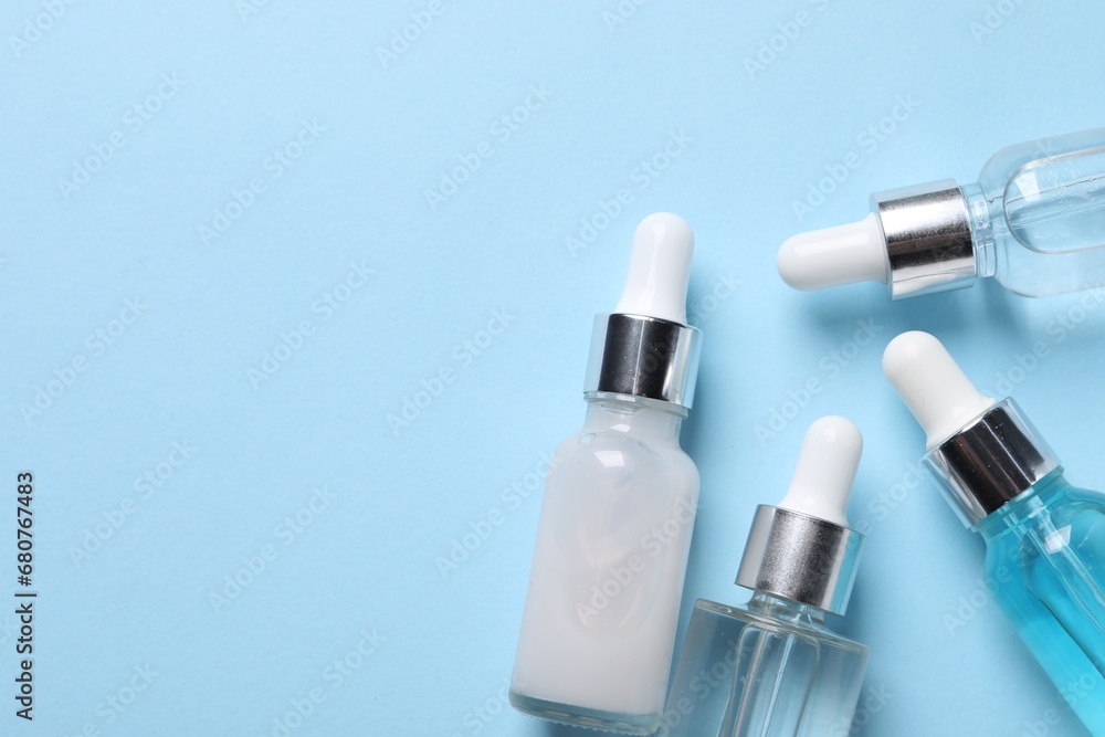 Many bottles of cosmetic serum on light blue background, flat lay. Space for text Many bottles of cosmetic serum on light blue background, flat lay. Space for text