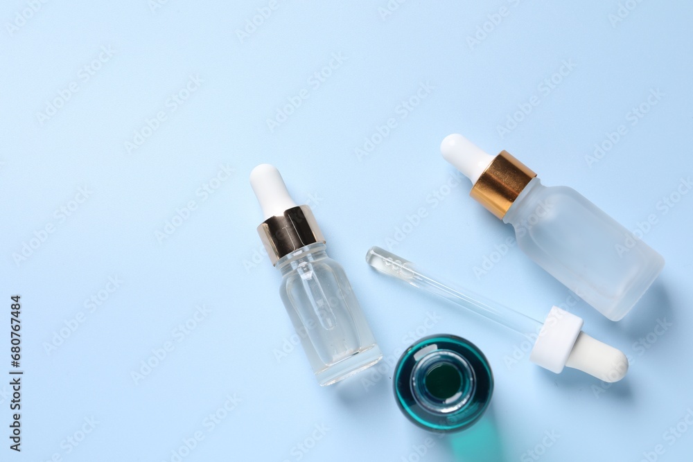Bottles of cosmetic serum on light blue background, flat lay. Space for text Bottles of cosmetic serum on light blue background, flat lay. Space for text