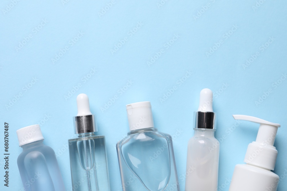 Many different bottles of cosmetic serum on light blue background, flat lay. Space for text Many different bottles of cosmetic serum on light blue background, flat lay. Space for text