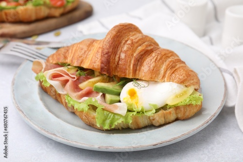 Delicious croissant with prosciutto, avocado and egg on white table