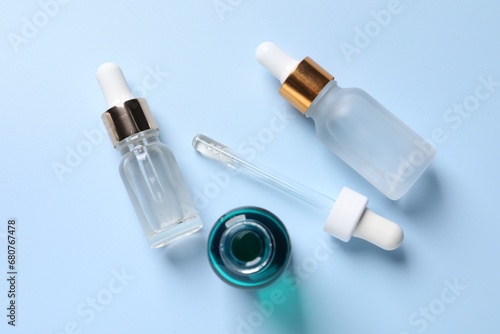 Bottles of cosmetic serum on light blue background, flat lay