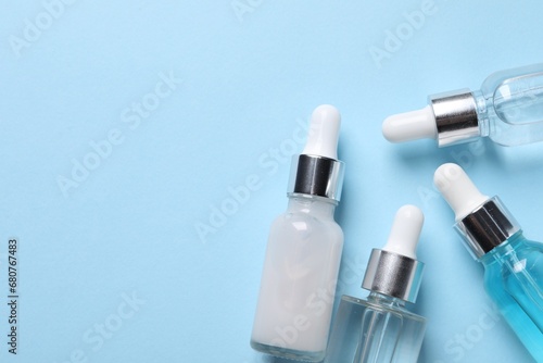 Many bottles of cosmetic serum on light blue background, flat lay. Space for text