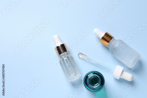 Bottles of cosmetic serum on light blue background, flat lay. Space for text
