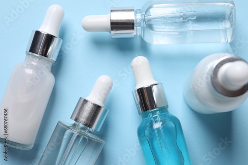 Many different bottles of cosmetic serum on light blue background, flat lay