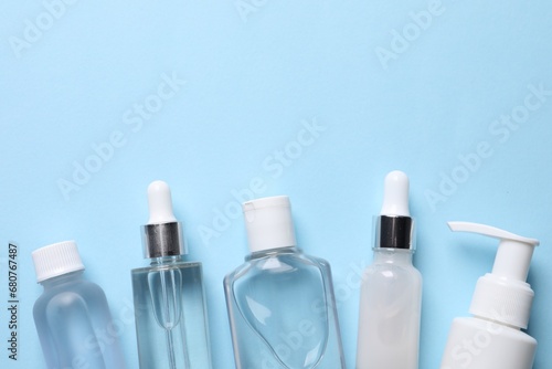 Many different bottles of cosmetic serum on light blue background, flat lay. Space for text