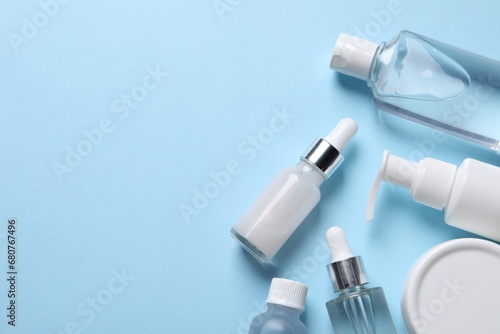 Many different bottles of cosmetic serum on light blue background, flat lay. Space for text