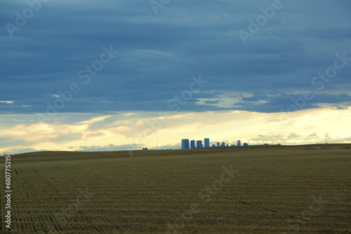 Calgary cityline with warm yellow agriculture field, cloudy sky with sun peaking out