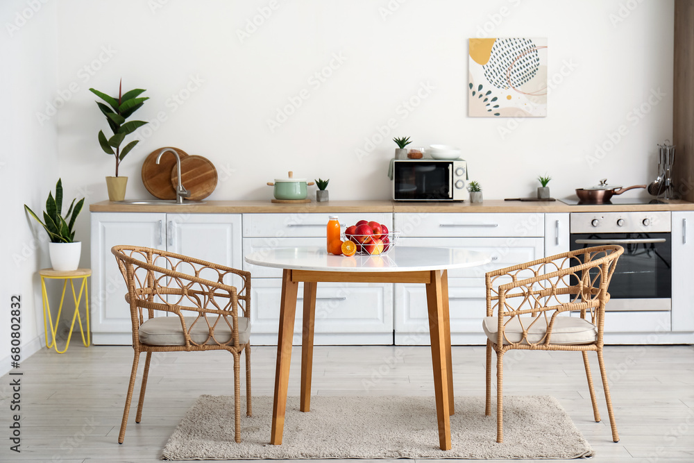Obraz premium Interior of modern kitchen with fruit basket and glass of juice on dining table