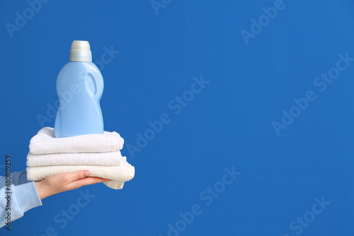 Female hands holding stack of clean towels with laundry detergent bottle on blue background photo