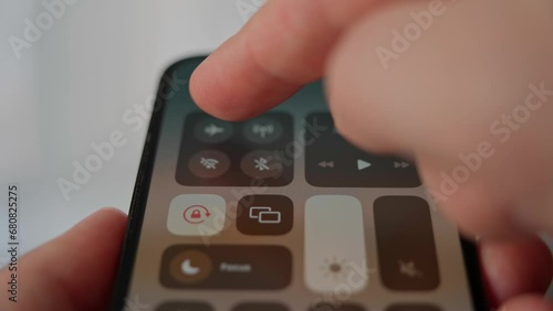 A man swipes down on the screen of his phone to turn on airplane mode. An airline passenger prepares for a flight by turning off his mobile phone.