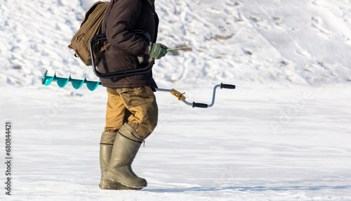 A man with a drill on the ice while fishing