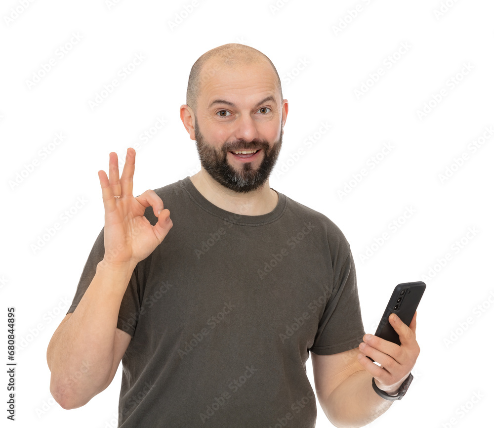 Portrait oh happy man with beard wearing brown t-shirt take selfie and make ok okay gesture, isolated on white background. Bald forty year old guy holding cell phone and posing in studio Portrait oh happy man with beard wearing brown t-shirt take selfie and make ok okay gesture, isolated on white background. Bald forty year old guy holding cell phone and posing in studio