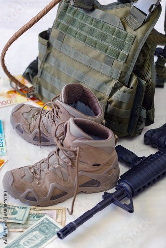 Bulletproof vest, money banknotes USA american dollar bills with israeli NIS , rifle and worn hiking boots on white floor. Military uniform protected with body armor, assault rifle, machine gun 16mm