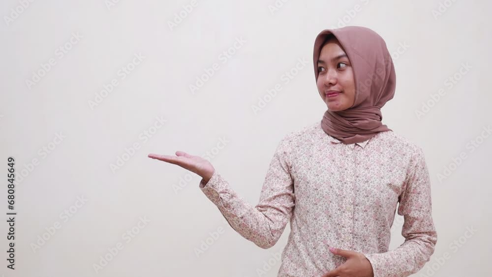 Happy young asian muslim woman standing while presenting something beside her on empty space. Isolated on white background Happy young asian muslim woman standing while presenting something beside her on empty space. Isolated on white background