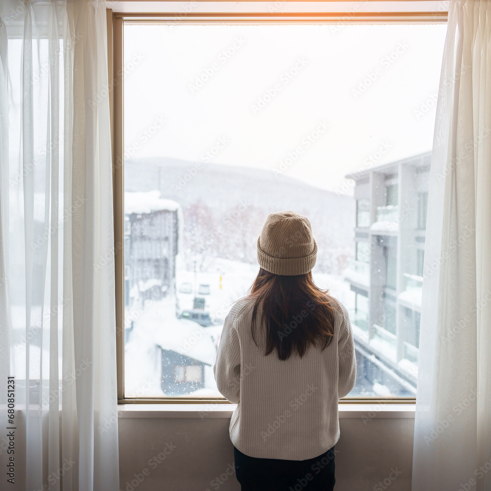 young woman in sweater looking through the window in winter season, happy female rising arms and stretching after waking at apartment or home in the morning. Lifestyle and Relaxing concepts young woman in sweater looking through the window in winter season, happy female rising arms and stretching after waking at apartment or home in the morning. Lifestyle and Relaxing concepts