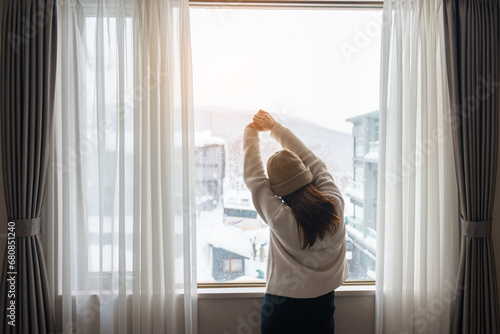 Free Download young woman in sweater looking through the window in winter season, happy female rising arms and stretching after waking at apartment or home in the morning. Lifestyle and Relaxing concepts - GFXLoad