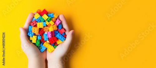 Hands holding colorful toy plastic bricks, blocks for building toys on yellow background