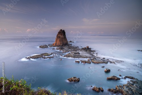 A large and tall rock is located in the middle of the sea surrounded by other small rocks. View icon from Papuma Beach Jember photo