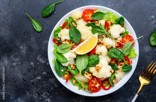 Healthy fresh vegan salad of cauliflower, baked paprika, cherry tomatoes and spinach with walnuts, dark table background, top view