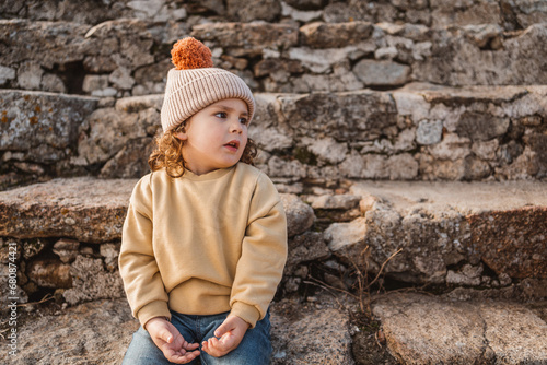 close up portrait of little fashionable boy with hat in earth tones, medieval stone castle background
