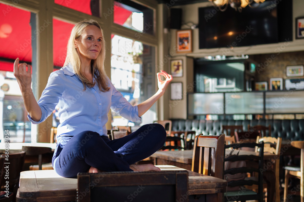 Blond businesswoman sitting and doing yoga on table in coffee shop Blond businesswoman sitting and doing yoga on table in coffee shop