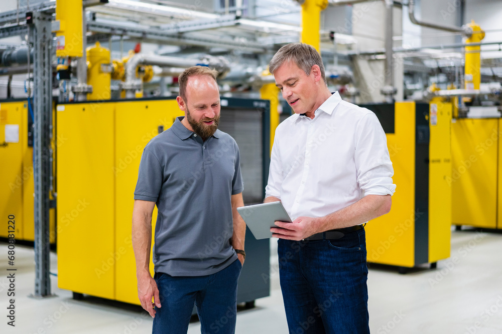 Employee and businessman with digital tablet talking in factory Employee and businessman with digital tablet talking in factory