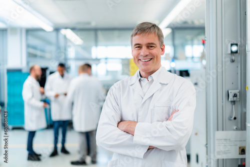 Technician in white lab coat standing in electronics factory with arms crossed photo