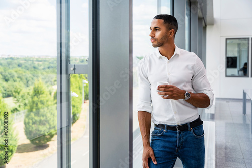 Casual businessman looking out of window holding cup of coffee photo