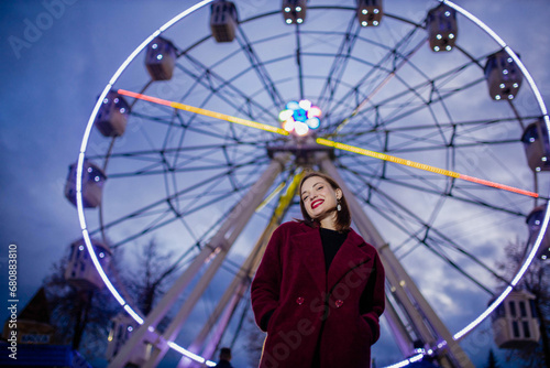beautiful woman in burgundy coat in amusement park in winter evening