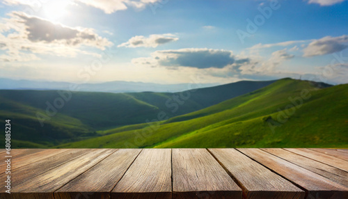 Wooden table in front of blurred green hills with cloudy sky. For product showing
