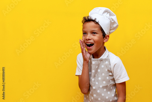 african american boy in uniform and chef's hat announces loudly and shouts on yellow isolated background photo