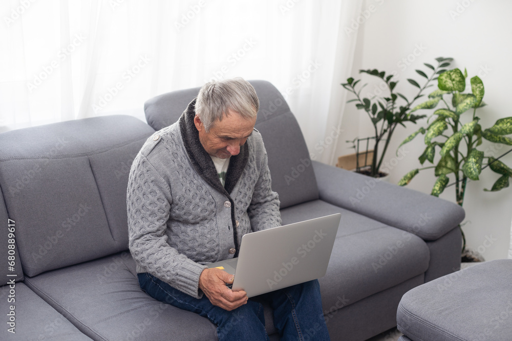 Older man sitting on sofa, smiling at computer screen at home Older man sitting on sofa, smiling at computer screen at home