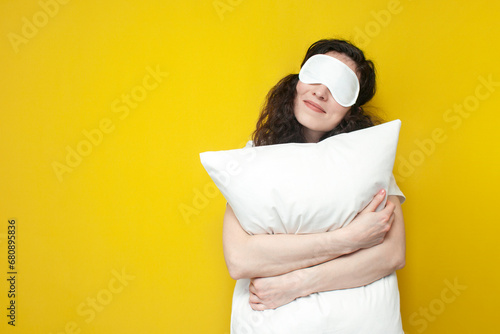 woman in sleep mask hugs white soft pillow on yellow background and sleeps, the concept of healthy sleep © Богдан Маліцький
