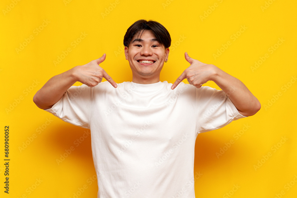 proud young asian guy in white t-shirt smiling and pointing to himself over yellow isolated background proud young asian guy in white t-shirt smiling and pointing to himself over yellow isolated background