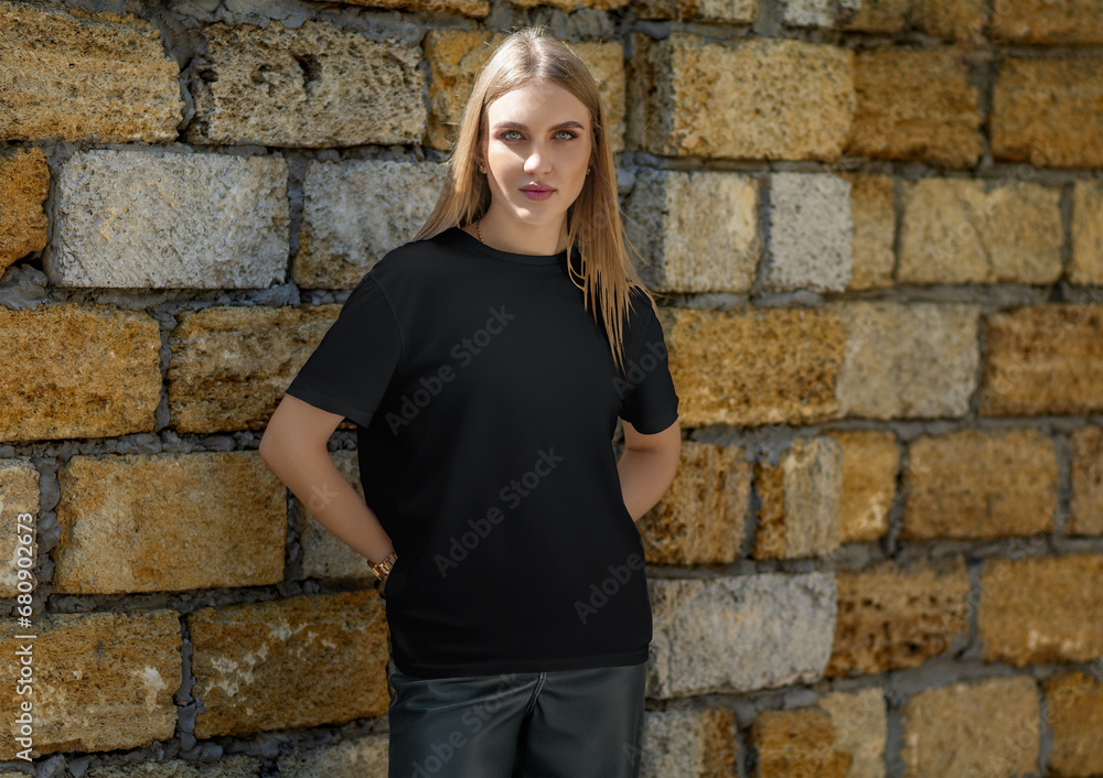Black t-shirt template on a fashionable blonde on the background of a brick wall, clothes on the street, front.