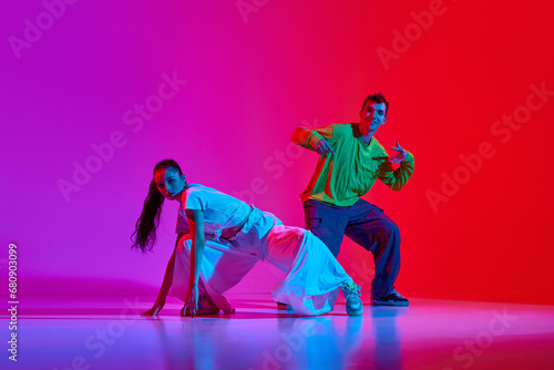 Fototapeta Naklejka Na Ścianę i Meble -  Creative flow. Young man and woman in motion, dancing hip hop against pink red background in neon light. Concept of hobby, action, street style, contemporary dance, youth, fashion