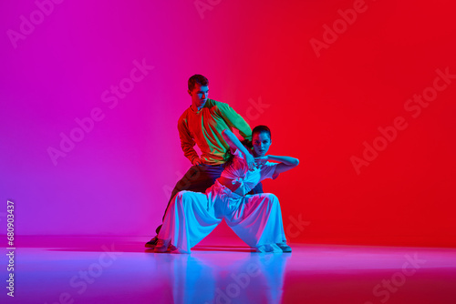 Freestyle performance. Young man and woman in motion, dancing hip hop against pink red background in neon light. Concept of hobby, action, street style, contemporary dance, youth, fashion