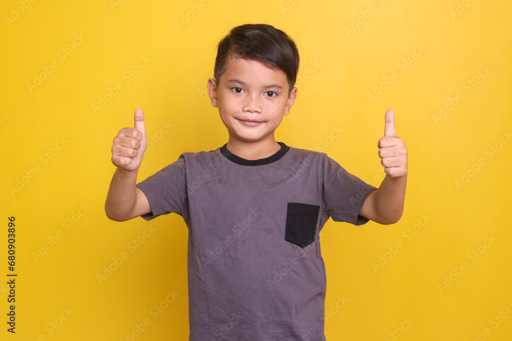Handsome Asian boy in casual t-shirt showing two thumbs up at camera isolated on yellow background Handsome Asian boy in casual t-shirt showing two thumbs up at camera isolated on yellow background