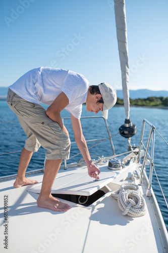 Young guy in white shirt and cap on the yacht fixing a rope