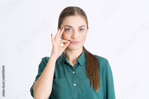 A woman's lips are sealed with a promise! Attractive young woman keeps her mouth shut, makes a zip gesture, hints to the interlocutor to be silent isolated on a white studio background