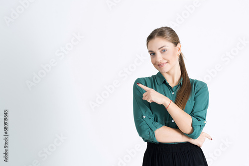 Look at this. Attractive young woman points her finger at an empty copy space for an advertisement isolated on a white studio background