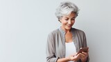 stylish senior woman with grey hair talking online using smartphone, modern lifestyle of the elderly, on light pastel background with copy space