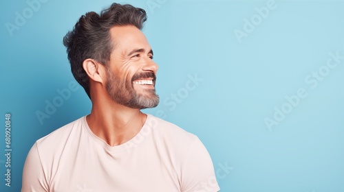handsome attractive man, smiling and laughing, looking to the right, wearing white t-shirt on pastel light blue background
